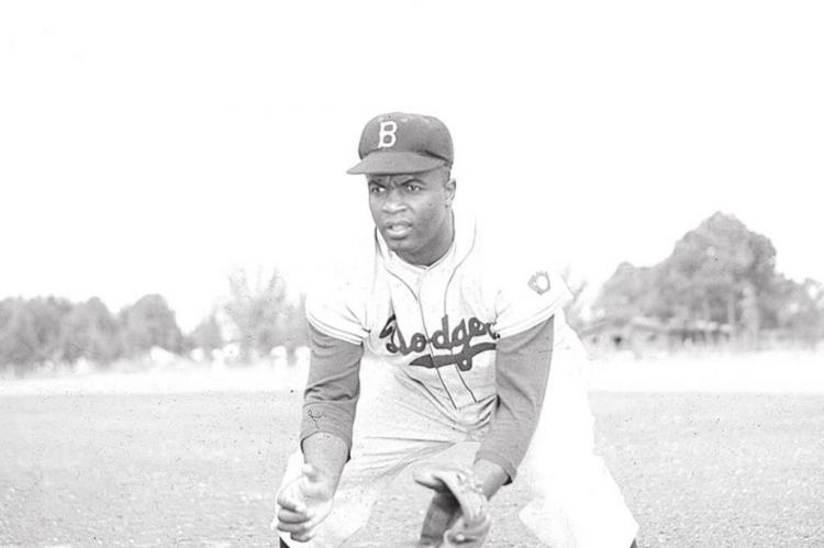 American professional baseball player Jackie Robinson (1919-1972) of the Brooklyn Dodgers, dressed in a road uniform, crouches by the base and prepares to catch a ball, 1951. Throughout the course of his baseball career Robinson played several positions on the infield as well as serving as outfielder. Keystone Hulton Archive | Getty Images | TNS